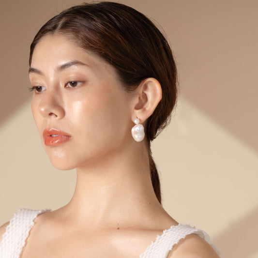 Dressed in a pristine white top, a woman exudes grace and refinement. The shimmering pearl earrings she wears enhance her allure.
