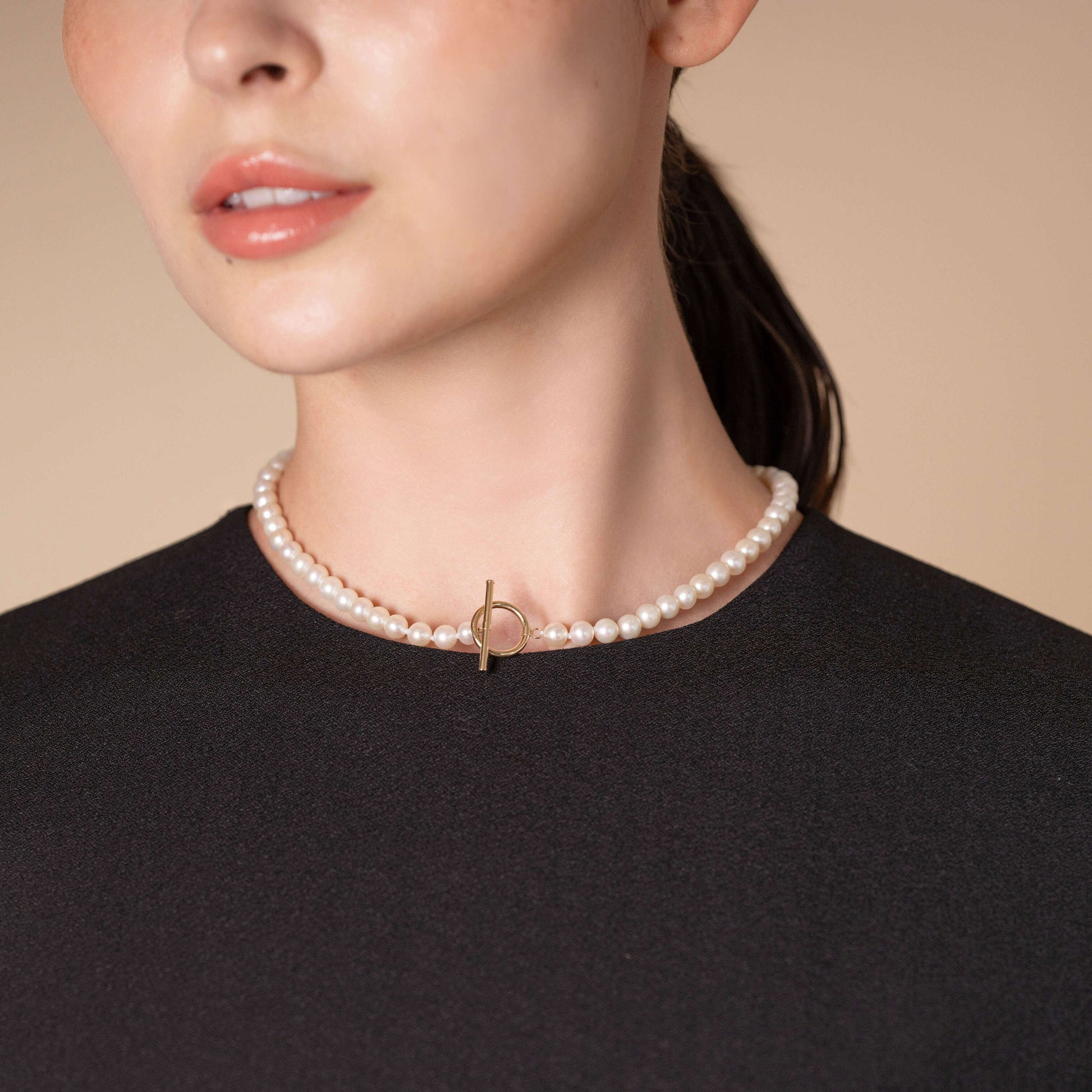 Elevate your look effortlessly - a woman donning a black top and a captivating Mantel Pearl Necklace Short.