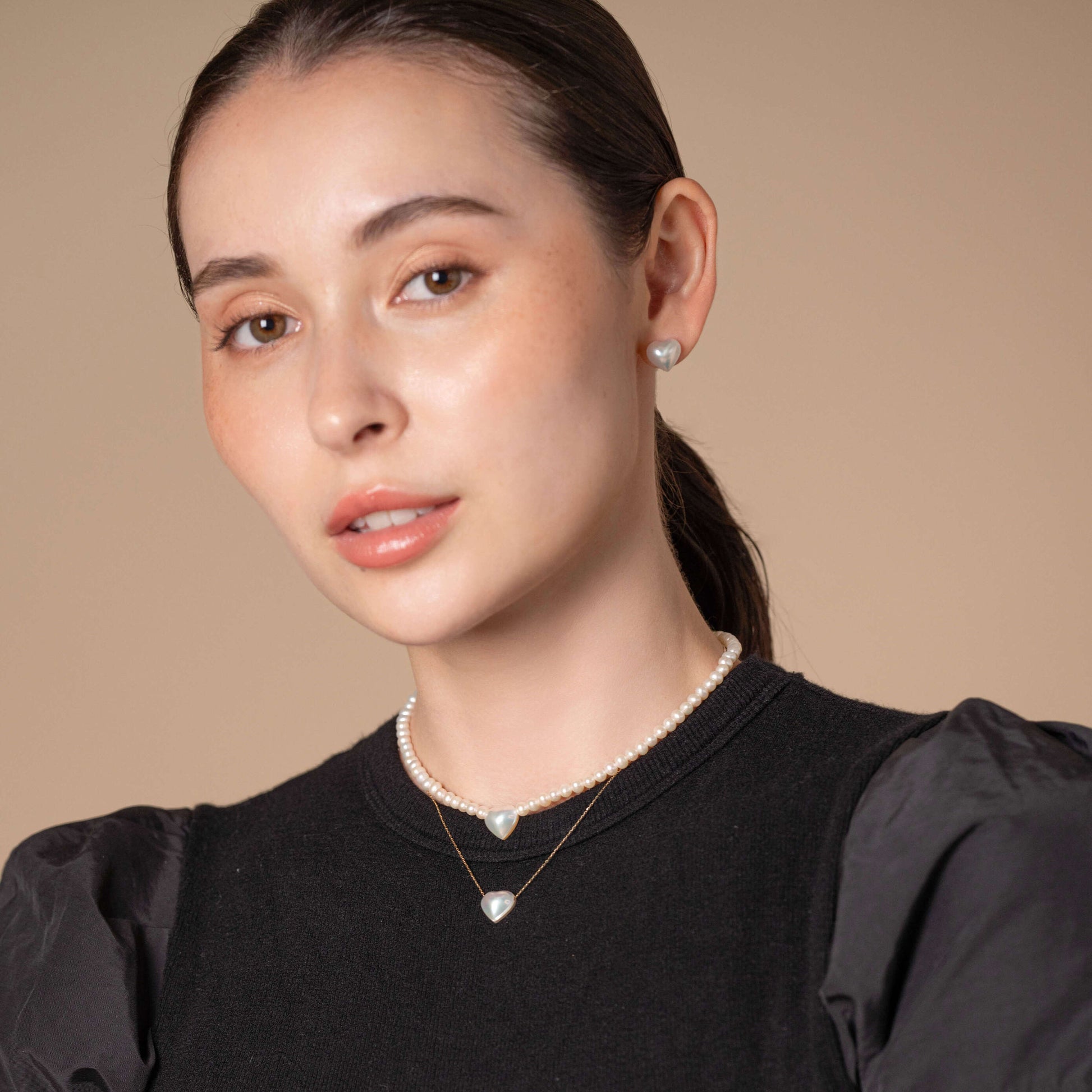 Elevate your fashion game with a woman donning a black top and an exquisite Heart Pearl Necklace.