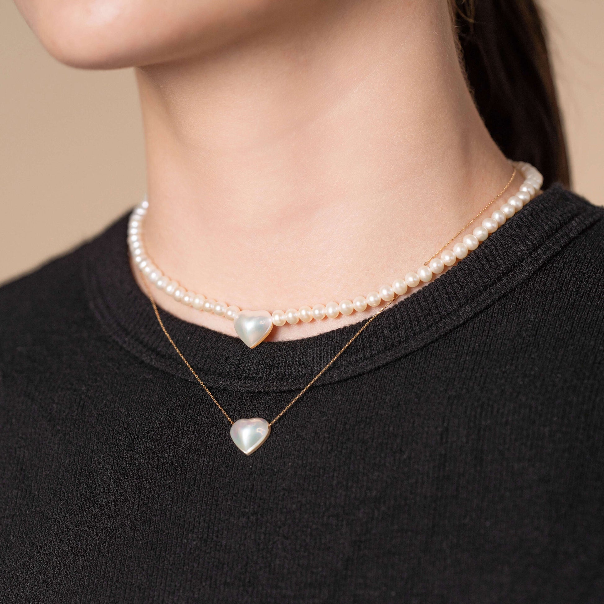 Indulge in elegance as you admire a woman in a black top adorned with a captivating Heart Pearl Necklace.