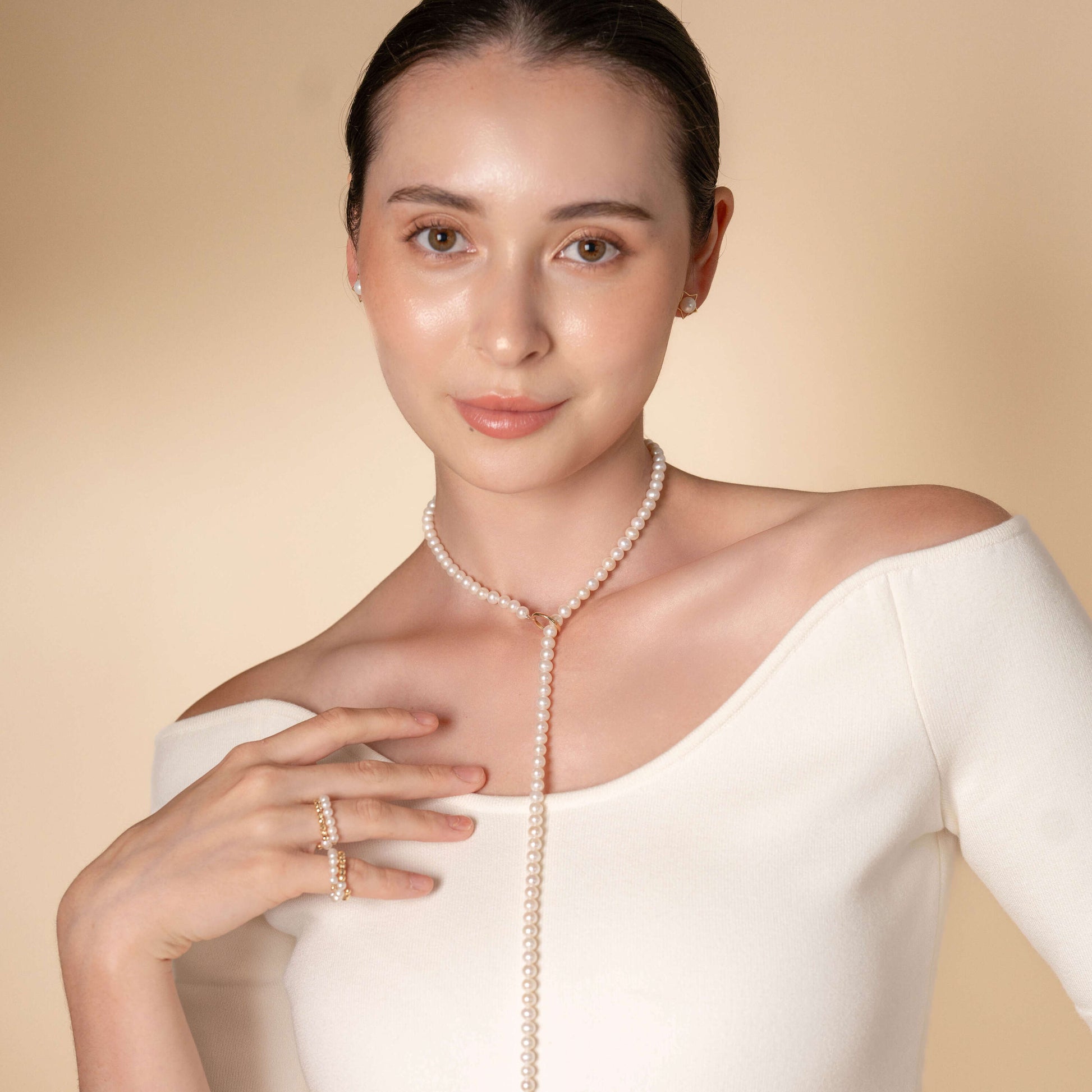 Elevate your style with a woman donning a white dress and a pearl necklace, beautifully paired with a mesmerizing Spiral Pearl x Gold Ring.