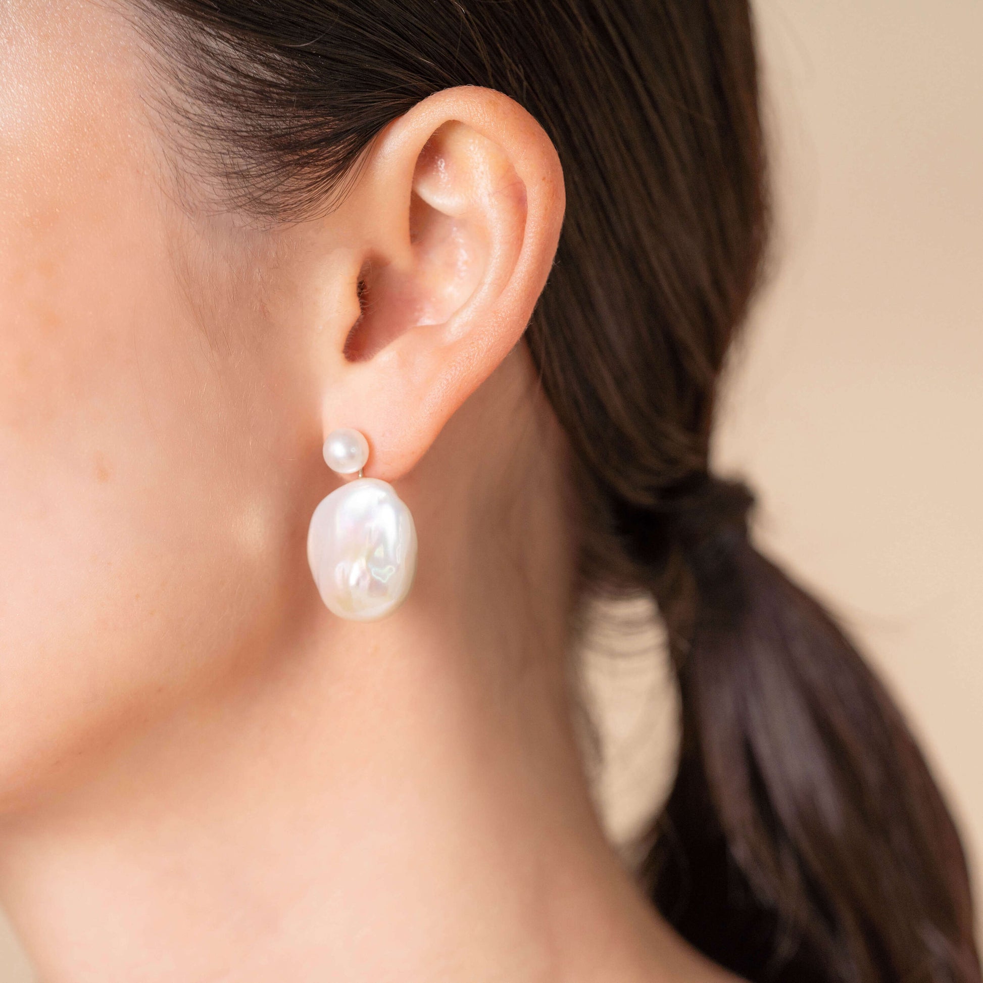 Add a touch of elegance to your outfit with a Baroque Pearl Charm Piercing and a pearl earring on a woman.