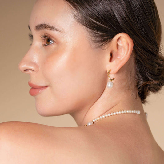 Enhance your elegance with a stunning woman adorned in a pearl necklace and earrings. Discover the timeless beauty of Pearl Dot x Gold Piercing.