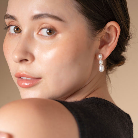 Enhance your style with a chic black top and elegant pearl earrings on a woman. Perfect for any occasion!
