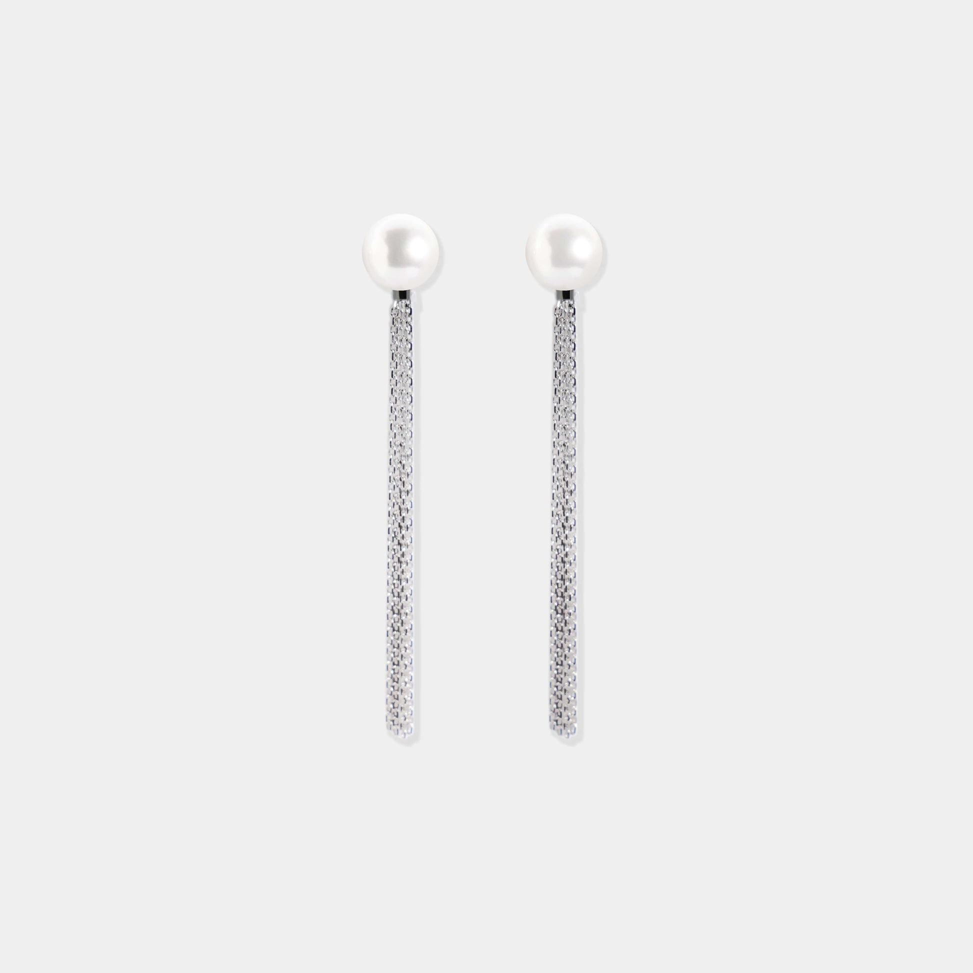 Elevate your look with a Pearl + Fringe Piercing! Witness a woman examining her ear by a window.