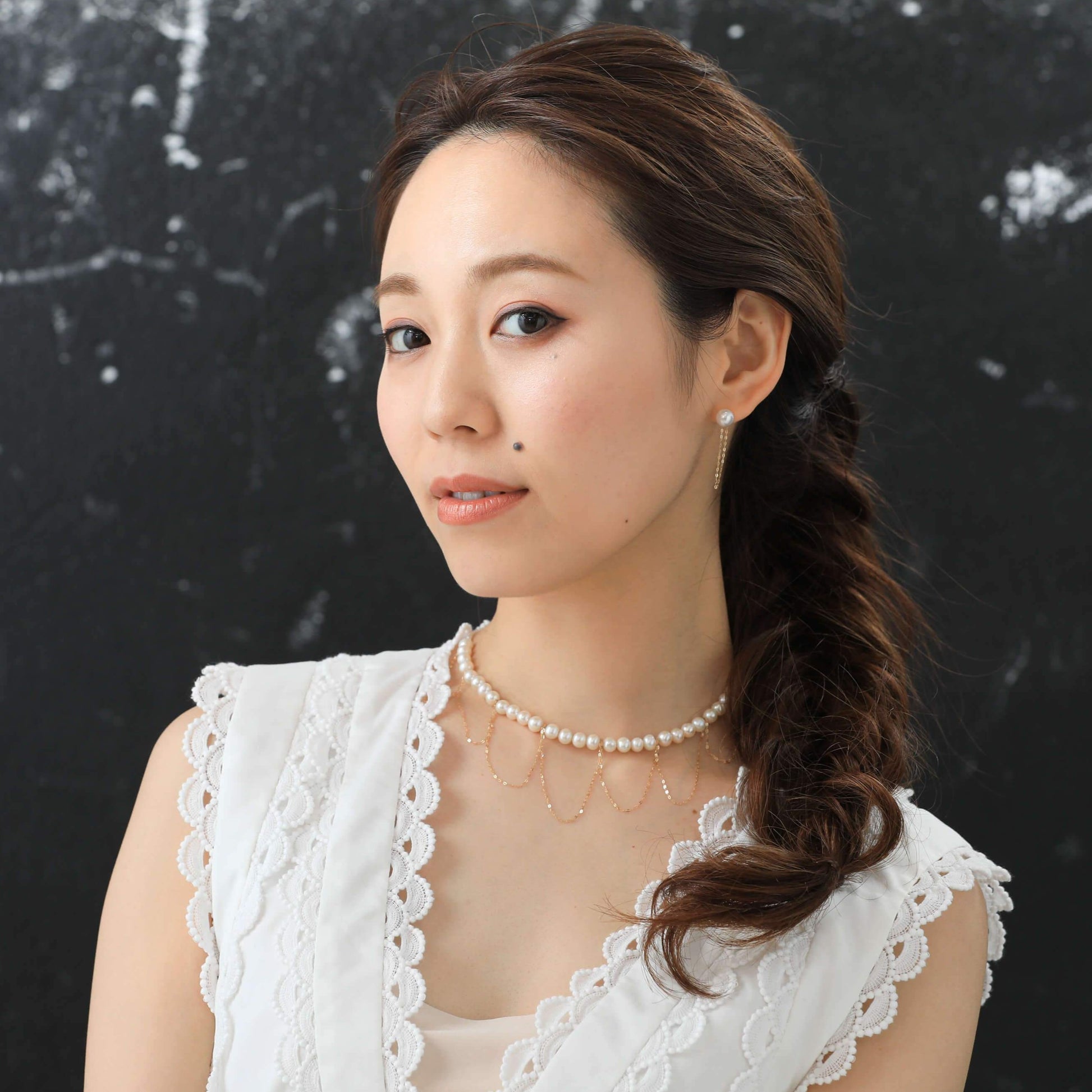 Elegant woman in white dress with draped gold and pearl necklace.