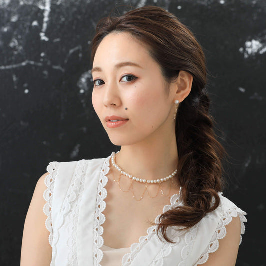 Elegant woman in white dress with draped gold and pearl necklace.