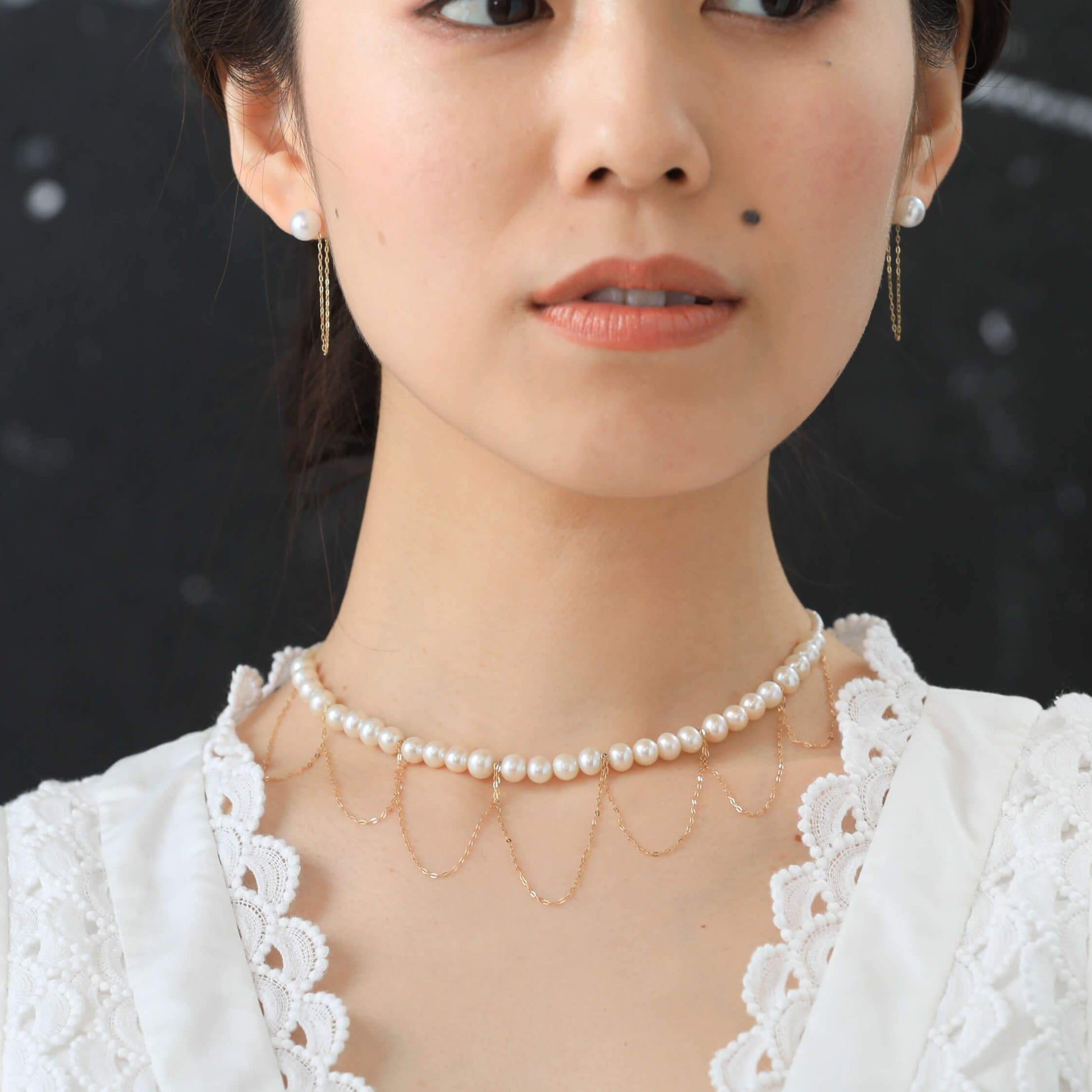 Stylish lady in white dress accessorized with gold and pearl necklace.