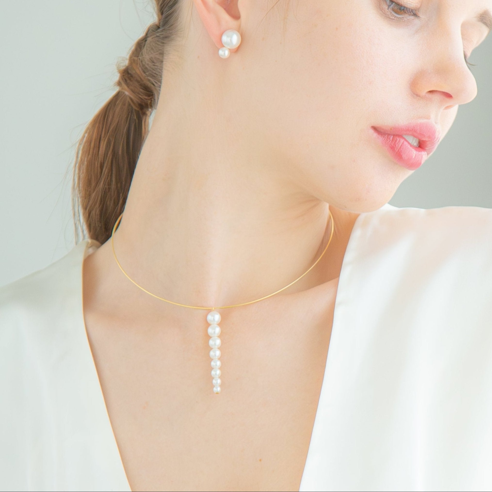 A woman dons a white top, highlighted by a sophisticated necklace of freshwater pearls and 18K yellow gold.