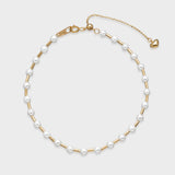Gold pearl bracelet with evenly spaced white pearls on a textured gold chain and adjustable clasp with heart charm.
