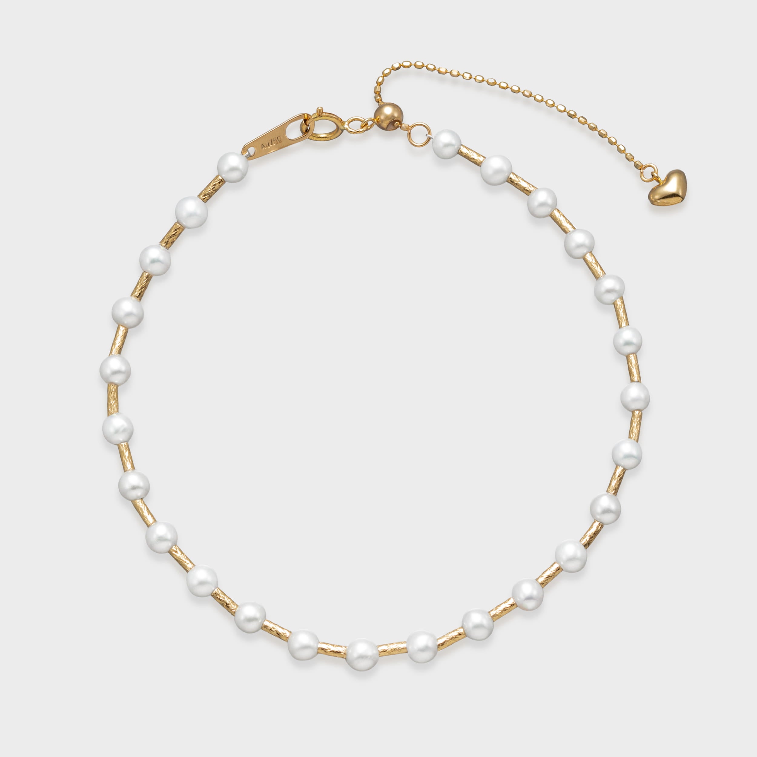 Gold pearl bracelet with evenly spaced white pearls on a textured gold chain and adjustable clasp with heart charm.