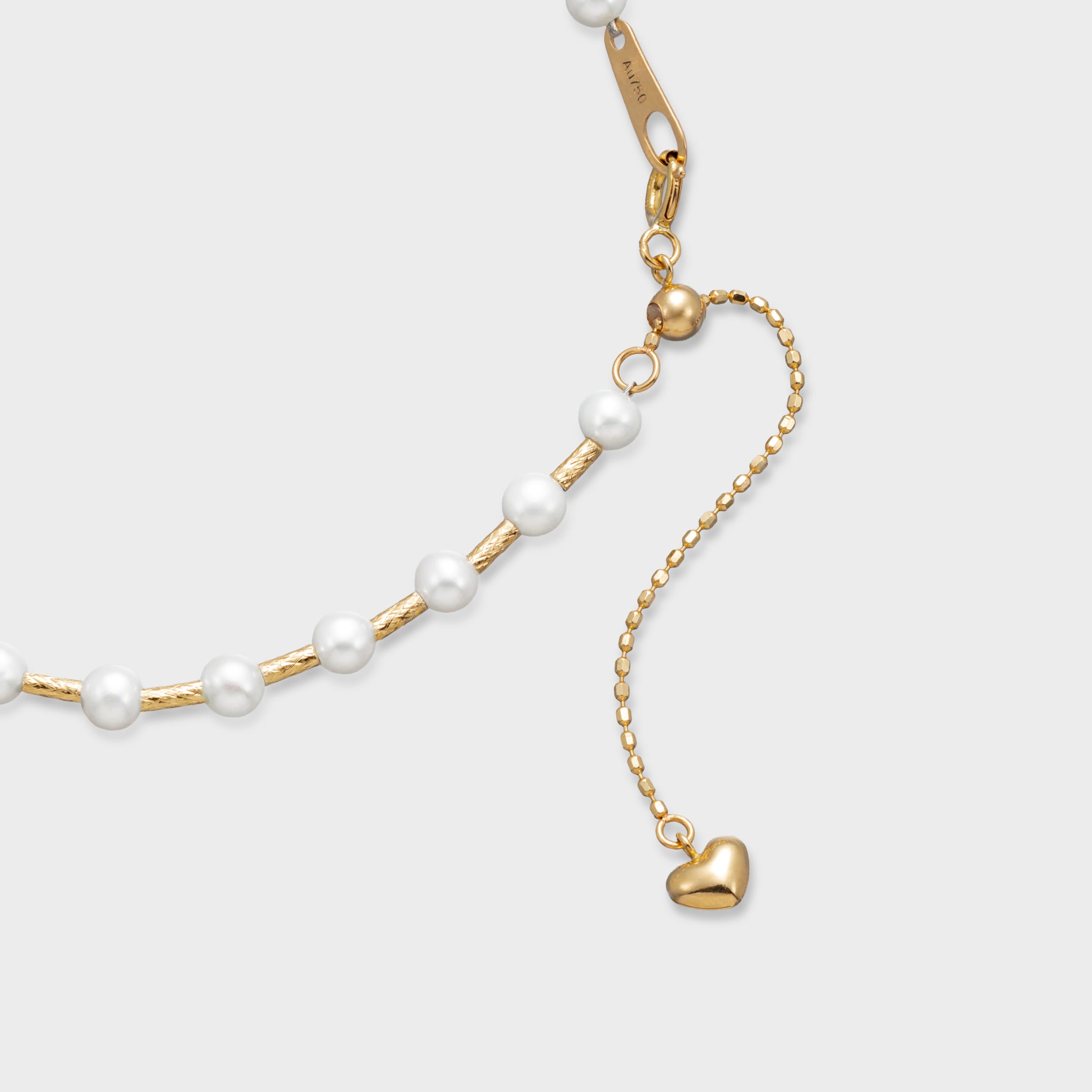 Gold pearl bracelet with evenly spaced white pearls on a textured gold chain and adjustable clasp with heart charm.