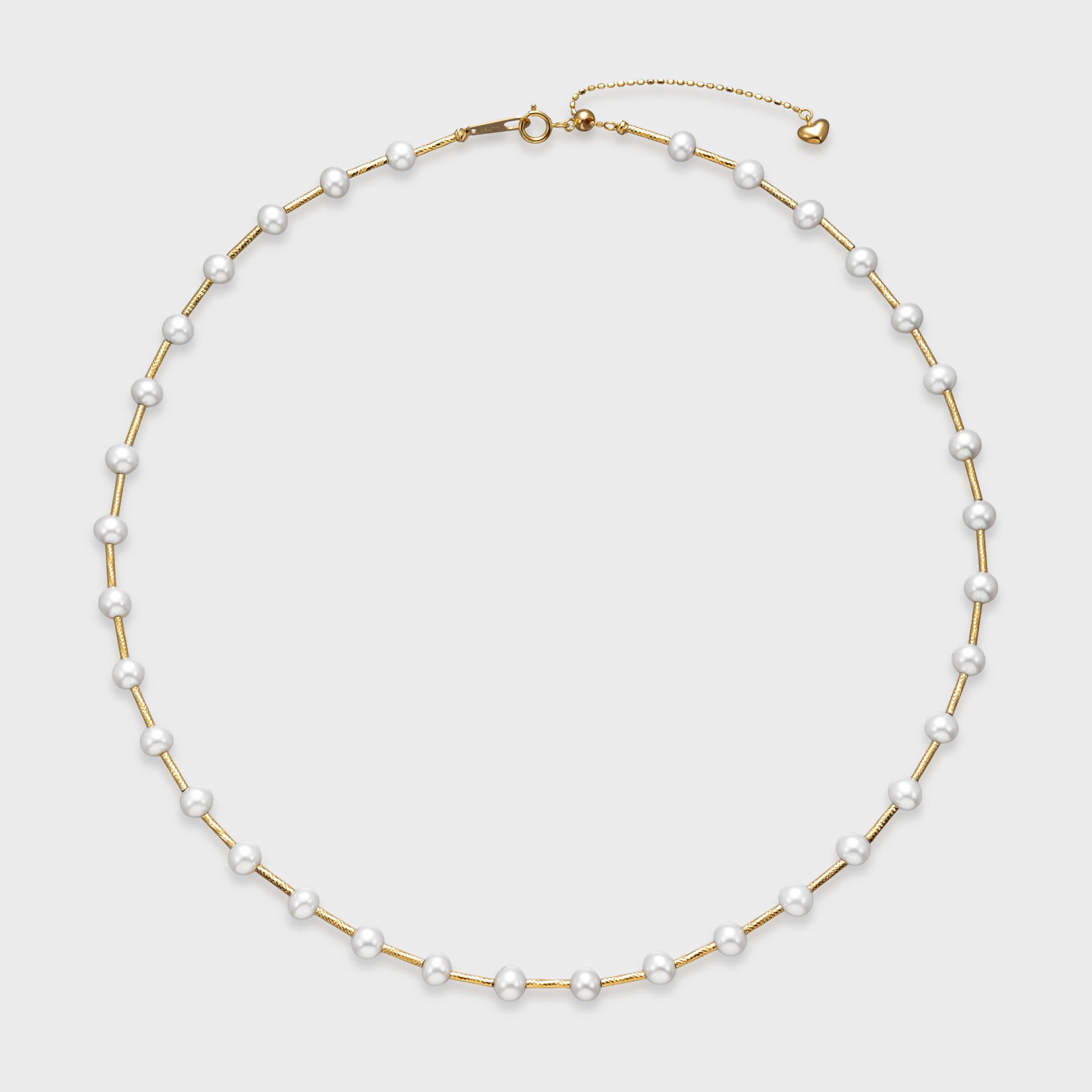 Gold pearl necklace with evenly spaced white pearls on a textured gold chain and adjustable clasp with heart charm.