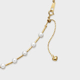Gold pearl necklace with evenly spaced white pearls on a textured gold chain and adjustable clasp with heart charm.
