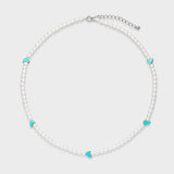 Delicate white pearl necklace with five turquoise enamel heart charms spaced evenly around the strand on a light gray background.