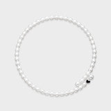 White oval freshwater pearl necklace with small black enamel heart charm accent on a light gray background.